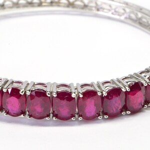 May include: A silver bangle bracelet with a row of oval-shaped ruby gemstones.