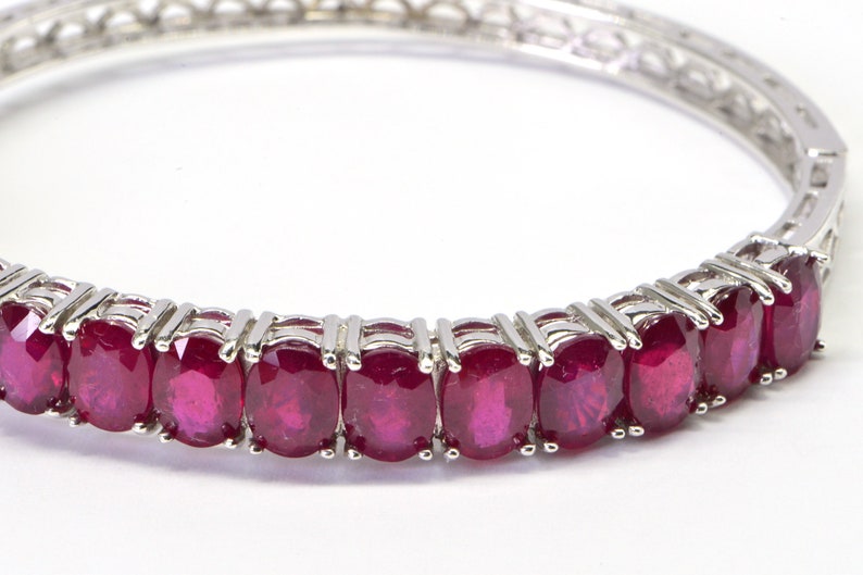 May include: A silver bangle bracelet with a row of oval-shaped ruby gemstones.