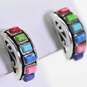 May include: A pair of silver hoop earrings with a rainbow of colorful stones. The stones are set in a silver band and are arranged in a row. The earrings are a beautiful and unique piece of jewelry.