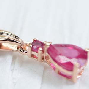 May include: A rose gold pendant necklace with a teardrop-shaped ruby gemstone. The pendant features a smaller ruby accent stone.