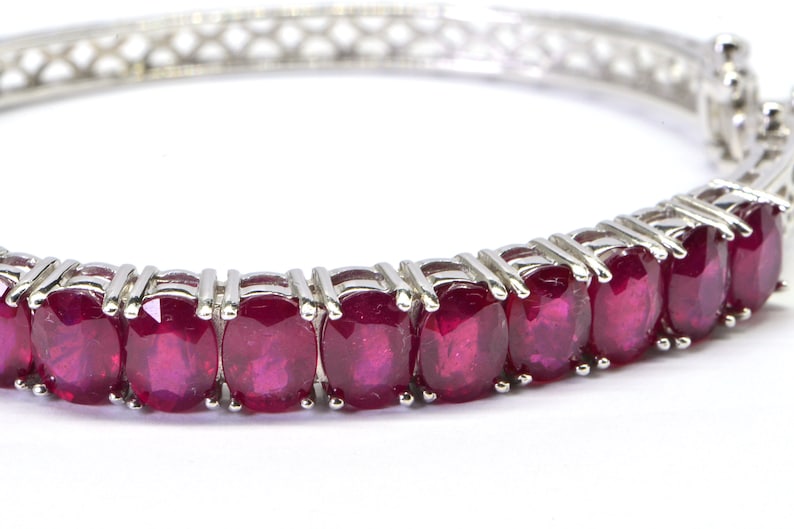 May include: A silver bangle bracelet with a row of oval-shaped ruby gemstones.