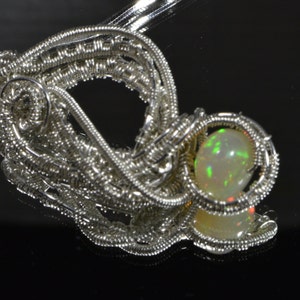 May include: A silver wire wrapped pendant featuring a round, iridescent opal gemstone.