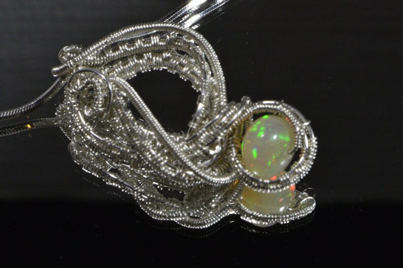 May include: A silver wire wrapped pendant featuring a round, iridescent opal gemstone.