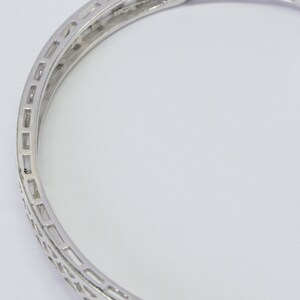 May include: A silver bangle bracelet with a delicate, intricate design. The bracelet is made of metal and has a polished finish.