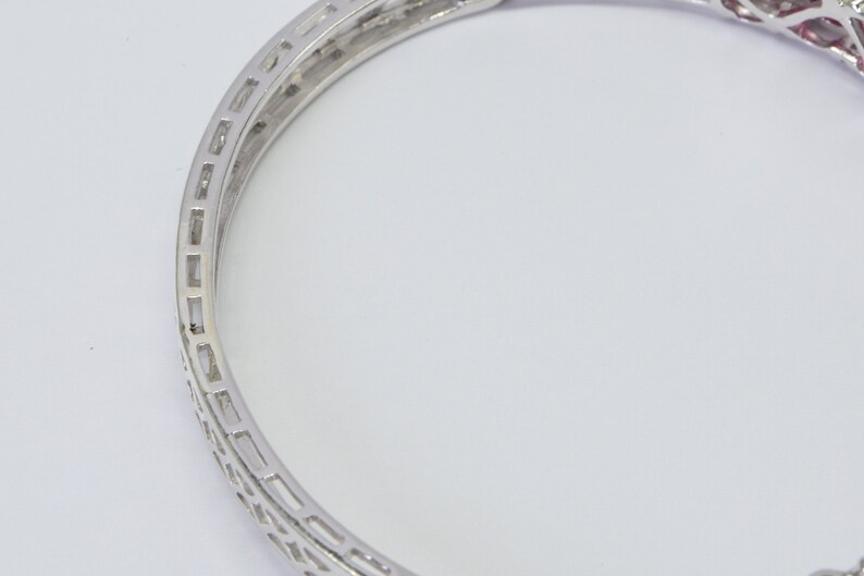 May include: A silver bangle bracelet with a delicate, intricate design. The bracelet is made of metal and has a polished finish.