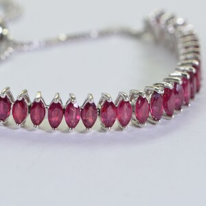 May include: A silver bracelet with a row of red marquise-shaped gemstones. The bracelet has an adjustable sliding clasp.