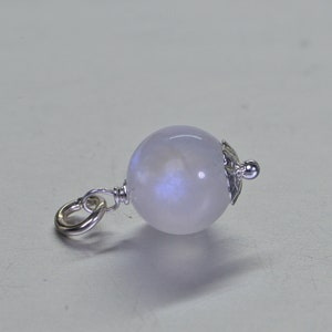 May include: A silver charm with a round, iridescent moonstone bead. The bead has a light blue and white color with a shimmery finish. The charm has a silver loop for attaching to a bracelet or necklace.