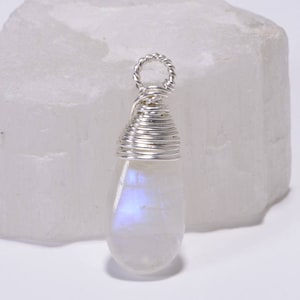 May include: A teardrop-shaped moonstone pendant wrapped in silver wire. The stone has a milky white color with iridescent blue and purple flashes.