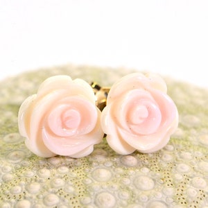May include: A pair of pink rose-shaped earrings with gold posts. The earrings are made of a smooth, white material and have a delicate, feminine design.