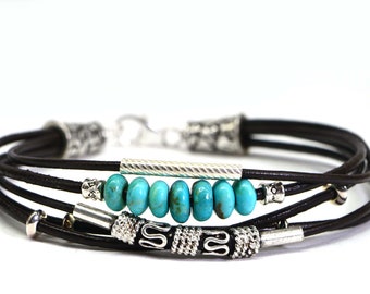 May include: A multi-strand leather bracelet with turquoise beads and silver accents. The bracelet has a hook clasp and is made of brown leather.