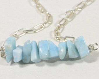 May include: A silver chain necklace with a light blue gemstone pendant. The pendant is made of several small, irregular shaped stones.