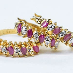 May include: Two gold rings with a row of marquise-shaped ruby and diamond stones. The rings are stacked on top of each other.
