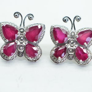 May include: A pair of silver butterfly earrings with red ruby stones and small white diamonds.