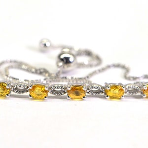 May include: A silver adjustable bracelet featuring oval-cut, golden-yellow gemstones. The gemstones are set in a silver chain with a sliding bead closure. The bracelet is displayed on a white background.