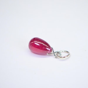 Puede incluir: Un colgante en forma de lágrima con una piedra preciosa de rubí rojo oscuro y una anilla de plata.