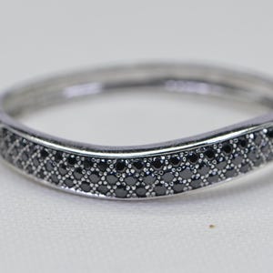 May include: A silver bangle bracelet with a curved design. The bracelet is set with a row of small black diamonds.