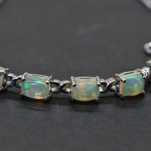 May include: A silver chain necklace with five rectangular opal stones. The stones are a pale green and white colour with a rainbow sheen.