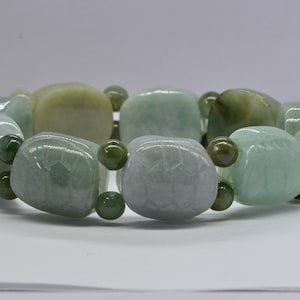 May include: A jade bracelet with green and white jade beads. The beads are carved with a design and are separated by smaller green beads.