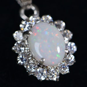 May include: A silver pendant featuring a white opal gemstone set within a halo of smaller clear gemstones.