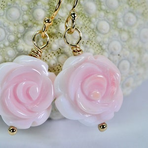 May include: A pair of gold earrings with pink shell rose flower charms. The earrings have a simple wire design and are perfect for everyday wear.