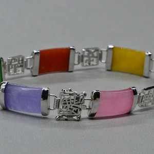 May include: A silver bracelet with a jade stone design. The bracelet features six different colored jade stones: green, orange, yellow, purple, pink, and blue.