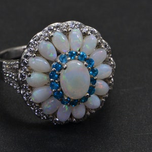 May include: A silver ring with a large white opal surrounded by smaller white opals and blue gemstones.