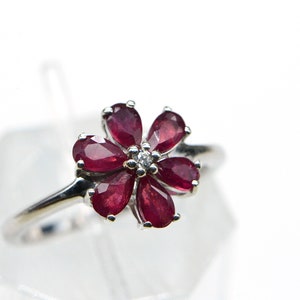 May include: A silver ring with a flower design featuring red rubies and a small diamond in the center.