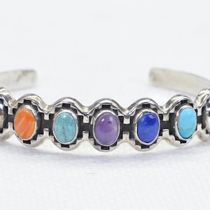 May include: A silver bracelet with seven oval-shaped gemstones in various colors, including green, orange, turquoise, purple, blue, and red.