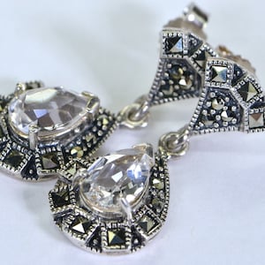 May include: A pair of silver earrings with clear pear-shaped stones set in a geometric design with black marcasite accents.