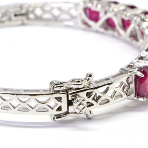 May include: A silver bangle bracelet with a delicate, openwork design and a row of red ruby gemstones.