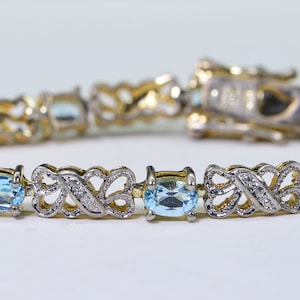 May include: A gold and silver bracelet with a delicate design featuring blue topaz gemstones. The bracelet has a clasp closure.