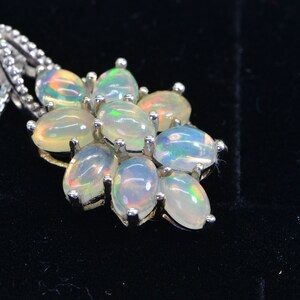 May include: A silver chain necklace with a pendant featuring a cluster of oval-shaped opal gemstones. The opals are iridescent with shades of white, green, and blue.