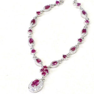 May include: A silver necklace with a pendant featuring a cluster of ruby stones. The necklace is adorned with a row of ruby stones set in silver.