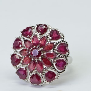 May include: A silver ring featuring a large cluster of red ruby gemstones set in a floral design.
