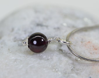 May include: A silver chain necklace with a dark red garnet gemstone pendant.