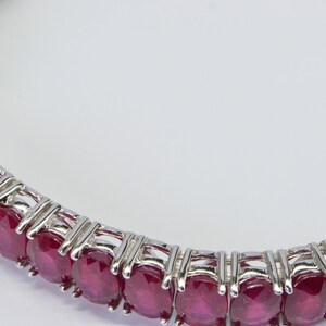 May include: A silver bangle bracelet with a row of oval-shaped ruby gemstones.