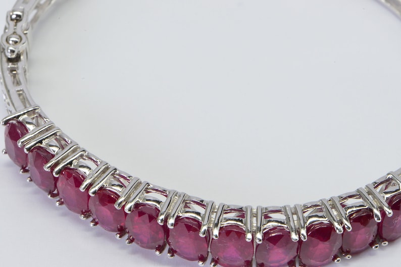 May include: A silver bangle bracelet with a row of oval-shaped ruby gemstones.