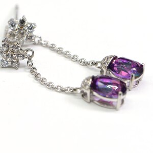 May include: A pair of silver dangle earrings with a purple oval gemstone and a cluster of clear cubic zirconia stones.