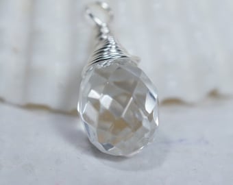 May include: A clear, faceted crystal pendant with a silver wire wrap. The teardrop-shaped crystal reflects light, showcasing its multiple facets. The pendant has a small loop at the top for hanging.