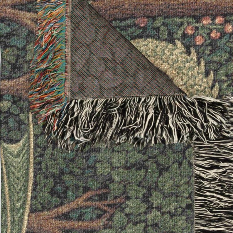 May include: A woven tapestry depicting a forest scene with green trees, brown branches, and red and orange fruit. The tapestry has a fringed edge with colourful threads and a dark grey backing.