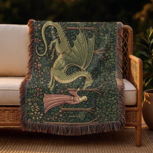 May include: A woven throw blanket depicting a dragon and a woman in a forest setting. The dragon is green and gold, with a woman in a pink dress. The background is dark green with floral and tree details. The blanket has a fringed edge.