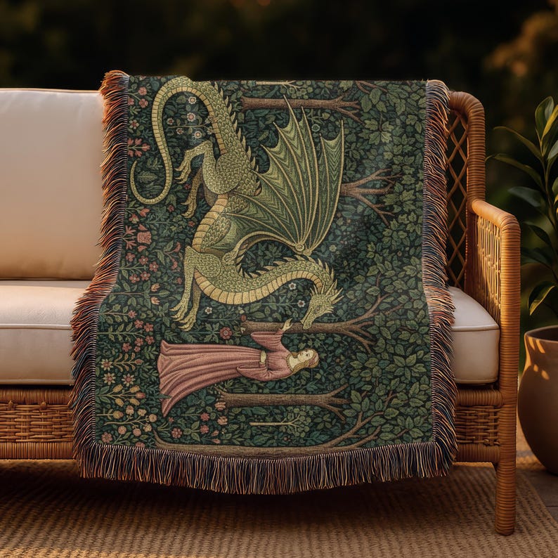 May include: A woven throw blanket depicting a dragon and a woman in a forest setting. The dragon is green and gold, with a woman in a pink dress. The background is dark green with floral and tree details. The blanket has a fringed edge.