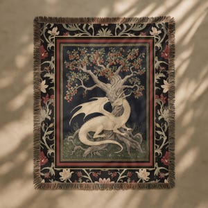 Può includere: Coperta tessuta con un'illustrazione dettagliata di un drago bianco sotto un albero con bacche rosse. Il design è incorniciato da un bordo floreale scuro e un bordo con frange. La tavolozza dei colori comprende nero, rosso e crema.