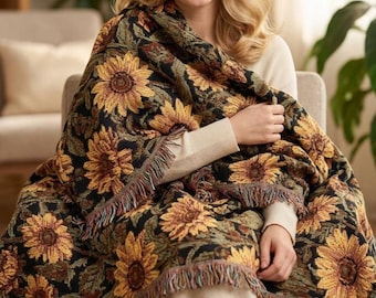 May include: A woven throw blanket featuring a repeating pattern of yellow sunflowers with brown centers and green leaves against a black background, finished with a decorative fringed edge along the bottom and sides of the textile fabric.