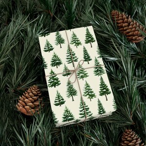 May include: Wrapped gift with cream-coloured paper patterned with green Christmas trees. The gift is tied with twine and rests on a bed of pine needles and pine cones, creating a festive holiday scene.