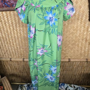 May include: A light green floral dress with a scoop neckline and short sleeves. The dress features a pattern of large blue and pink flowers with green leaves. The dress is displayed on a black mannequin.