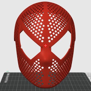 May include: A red mask with a web-like pattern of holes, featuring large eye openings and a nose section. The mask's design is reminiscent of a superhero's mask. The mask is likely made of plastic.