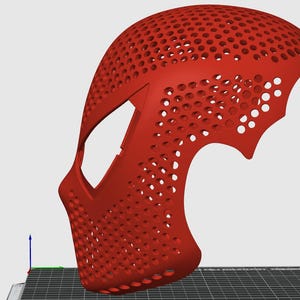 May include: A red, 3D-printed mask with a perforated design. The mask has a curved shape, covering the face and part of the head, with numerous small holes throughout. The design includes a stylized shape on the side.