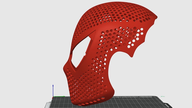 May include: A red, 3D-printed mask with a perforated design. The mask has a curved shape, covering the face and part of the head, with numerous small holes throughout. The design includes a stylized shape on the side.