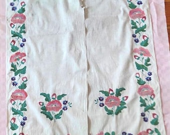 Puede incluir: Textil blanco con bordado floral. El bordado presenta flores y hojas rosas, rojas, verdes y azules. El textil está doblado por la mitad, con los bordes bordados a lo largo de los lados.